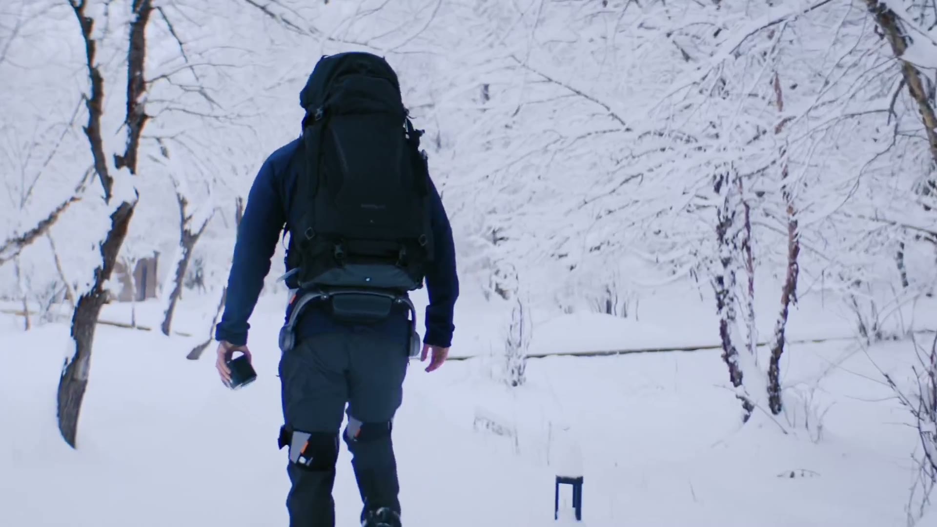 A hiker wearing a powered exoskeleton walking through a snowy forest